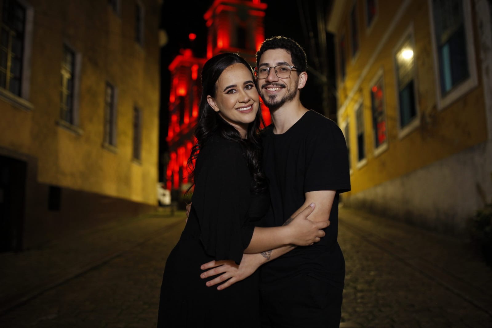 Bianca e Alan em frente a um prédio iluminado